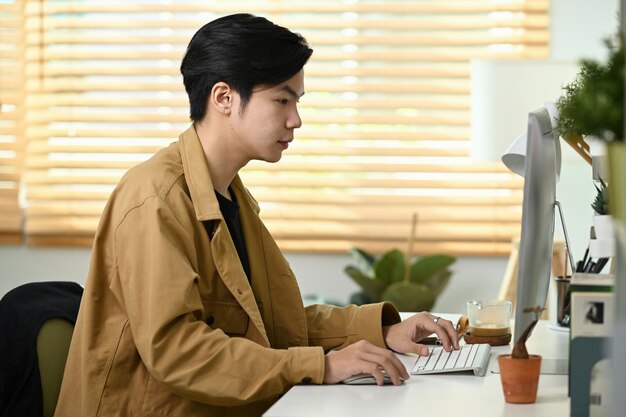 Bell'uomo asiatico che lavora con il computer in ufficio a casa.