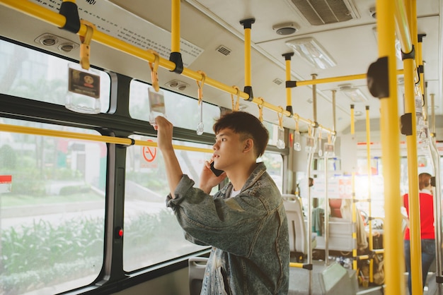 Bell'uomo asiatico in piedi in autobus cittadino e parlando al cellulare