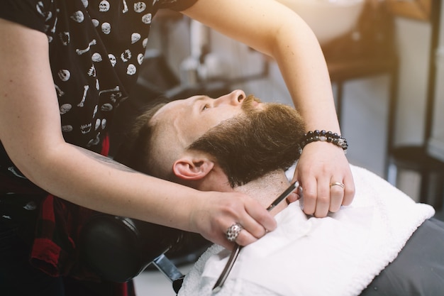 Bell&#39;uomo barbuto e con i baffi si fa la barba nel negozio di barbiere.