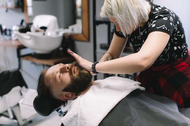 Bell&#39;uomo barbuto e con i baffi si fa la barba nel negozio di barbiere.