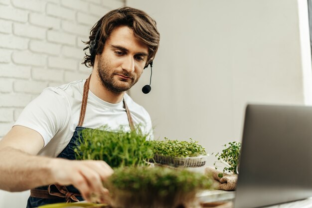 Bell'uomo barbuto vende germogli di piante e piantine online utilizzando laptop tramite videochiamata