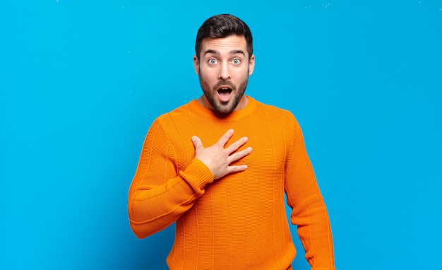 Bell'uomo biondo adulto che si sente scioccato, stupito e sorpreso, con la mano sul petto e la bocca aperta, dicendo chi, io?