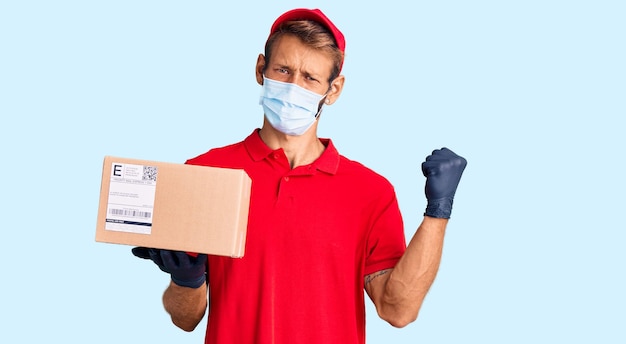 Bell'uomo biondo con la barba che tiene la scatola delle consegne indossando una maschera medica che urla orgoglioso celebrando la vittoria e il successo molto eccitato con le braccia alzate