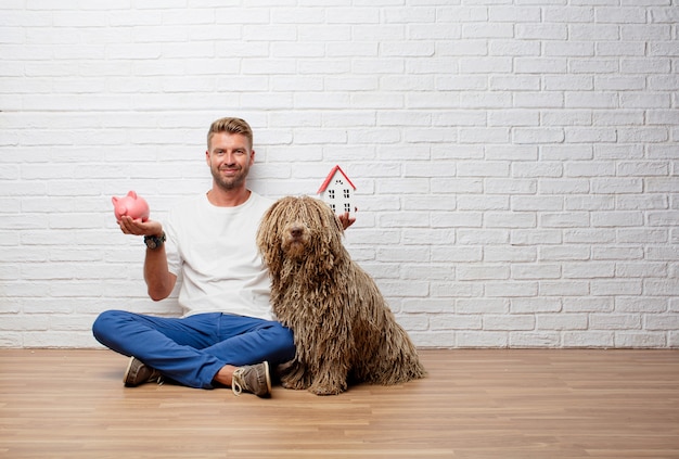 Bell&#39;uomo biondo con un cane, modello di casa e un salvadanaio