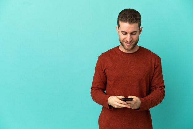 Bell'uomo biondo su sfondo blu isolato che invia un messaggio con il cellulare