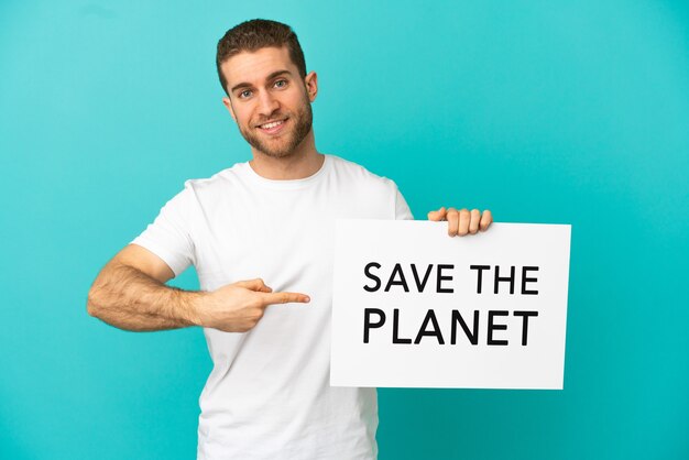 Bell'uomo biondo su sfondo blu isolato che tiene un cartello con il testo Salva il pianeta e lo indica