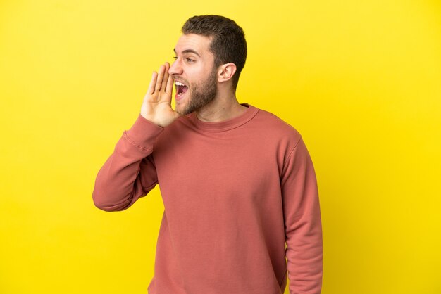 Bell'uomo biondo su sfondo giallo isolato che grida con la bocca spalancata di lato