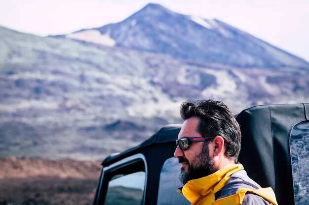 Bell'uomo caucasico adulto con barba e occhiali da sole e montagna - viaggio avventura persone concetto all'aperto con fuoristrada e attrezzature - stile di vita attivo