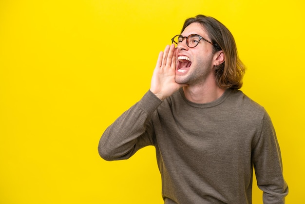 Bell'uomo caucasico isolato su sfondo giallo che grida con la bocca spalancata di lato