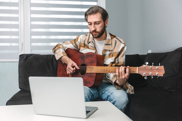Bell'uomo che impara a suonare lezioni online di chitarra acustica usando il laptop