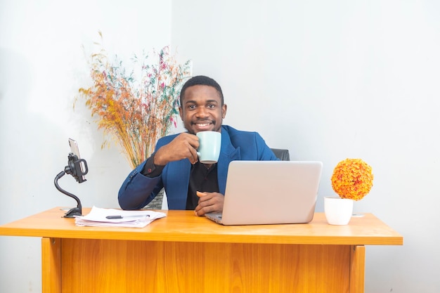 Bell'uomo che lavora utilizzando il computer portatile e beve una tazza di caffè con un'espressione sicura sul viso intelligente