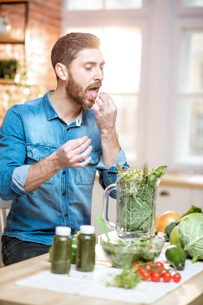 Bell'uomo che prova i prodotti mentre prepara un frullato vegetariano in cucina a casa