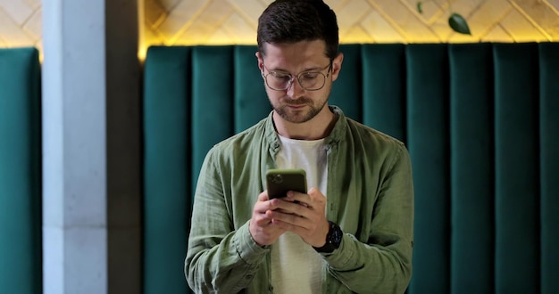 Bell'uomo che usa lo smartphone nel Cafe Uomo con gli occhiali che sorride controllando i social media e digitando il messaggio