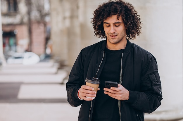 Bell'uomo con i capelli ricci che beve caffè per strada