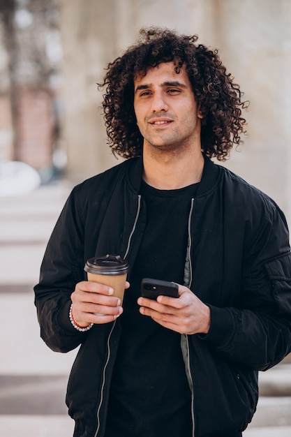 Bell'uomo con i capelli ricci che beve caffè per strada