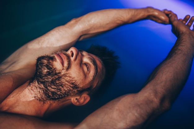 Bell'uomo con la barba che galleggia in un serbatoio pieno di acqua salata densa usata in meditazione, terapia e medicina alternativa.