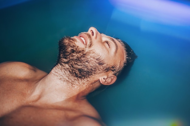 Bell'uomo con la barba che galleggia in un serbatoio pieno di acqua salata densa usata in meditazione, terapia e medicina alternativa.