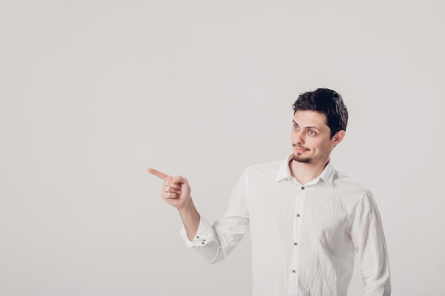 Bell'uomo con la barba che indica lo spazio della copia. giovane in camicia che punta via su uno sfondo grigio. luce soffusa