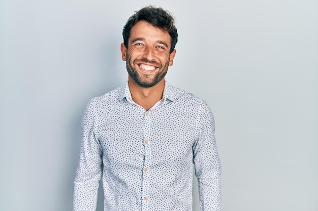 Bell'uomo con la barba che indossa una camicia casual elegante dall'aspetto positivo e felice in piedi e sorridente con un sorriso fiducioso che mostra i denti