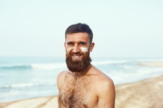 Bell'uomo con la barba in occhiali da sole, prendere il sole con crema solare corpo in estate