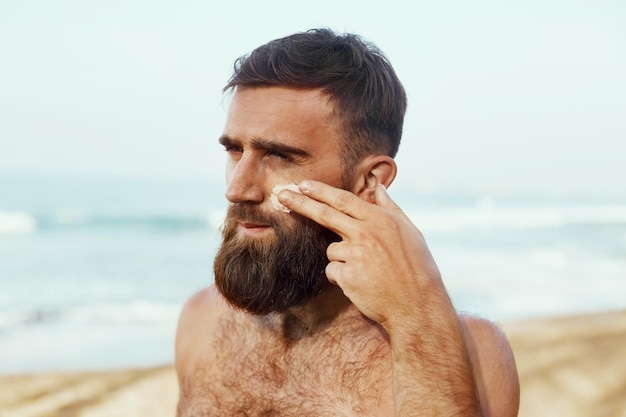 Bell'uomo con la barba in occhiali da sole, prendere il sole con crema solare corpo in estate