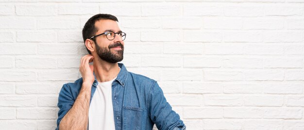 Bell&#39;uomo con la barba sul muro di mattoni bianchi pensando un&#39;idea