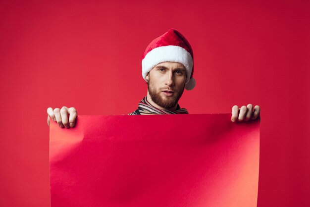 Bell'uomo con un cappello da Babbo Natale che tiene in mano uno striscione natalizio sfondo rosso