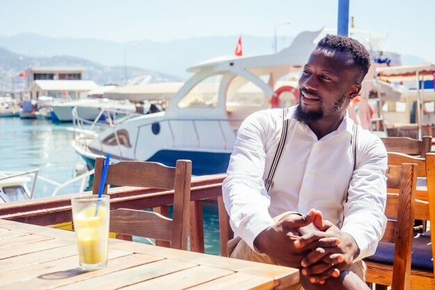 bell'uomo d'affari afroamericano con frullato sano in un caffè tropicale sulla spiaggia estiva in Turchia.