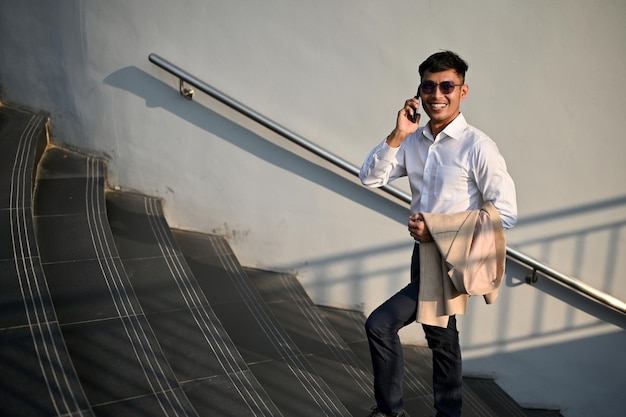 Bell'uomo d'affari asiatico che parla al telefono mentre cammina sulle scale in una città