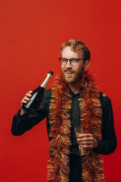 Bell'uomo dai capelli rossi con gli occhiali e un boa d'oro solleva un bicchiere di champagne Celebrazione del nuovo anno