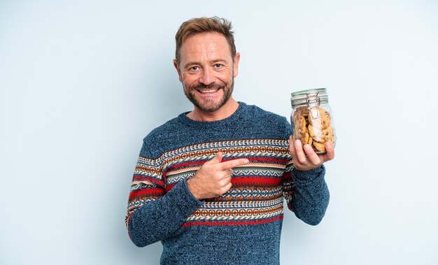 Bell'uomo di mezza età che sorride allegramente, si sente felice e indica il lato. bottiglia di biscotti