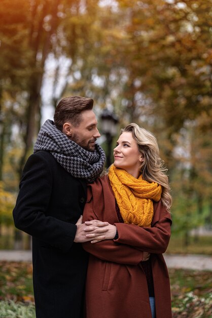 Bell'uomo e una donna abbracciati da dietro sorridono guardandosi l'un l'altro nel parco in autunno