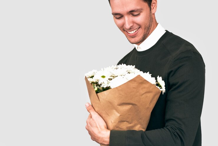 Bell'uomo felice sorridente offrendo un mazzo di fiori bianchi Modello maschile attraente con un mazzo di fiori che si prepara per un appuntamento con la fidanzata San Valentino Concetto di festa della mamma