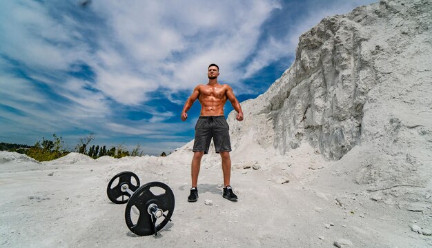 Bell'uomo forte che mostra i suoi muscoli che pubblicizzano uno stile di vita sano di sport attivo Culturista in posa all'aperto