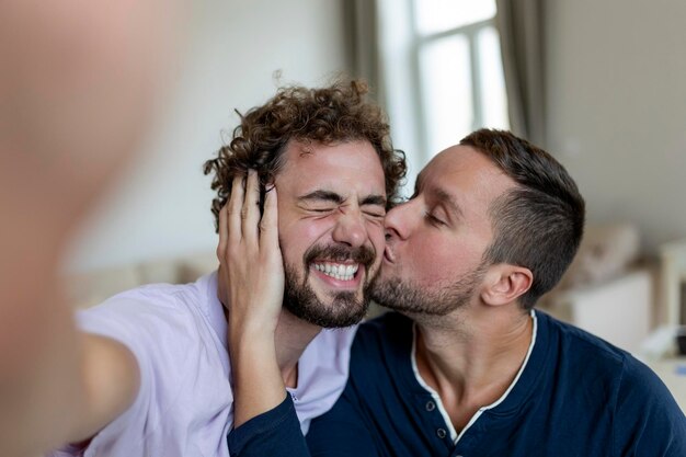 Bell'uomo gay seduto insieme a casa facendo un selfie con il cellulare Uomo gay con il suo partner seduto facendo un autoritratto usando lo smartphone