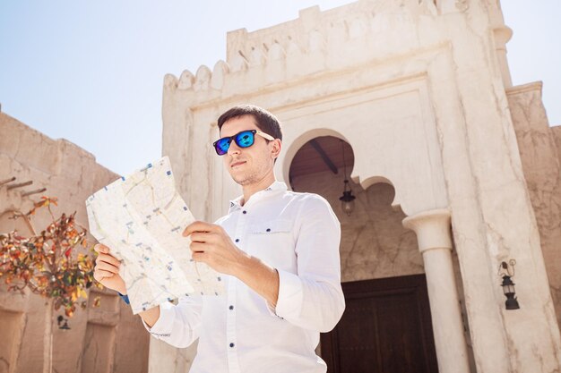 Bell'uomo in camicia bianca che guarda la mappa e cerca modi per scoprire nuove attrazioni nella famosa zona del vecchio Bur Dubai Creek Concetto di navigazione e luoghi turistici