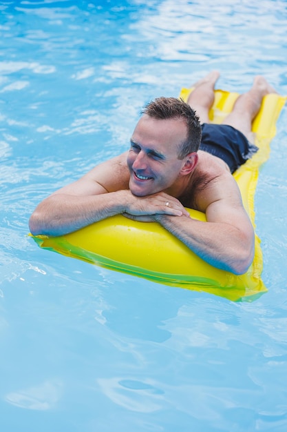 Bell'uomo in pantaloncini da bagno con un materasso giallo gonfiabile in piscina Vacanze estive in hotel