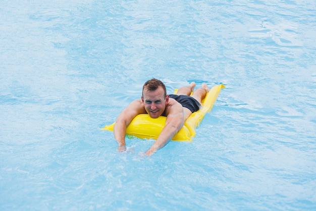 Bell'uomo in pantaloncini da bagno con un materasso giallo gonfiabile in piscina Vacanze estive in hotel