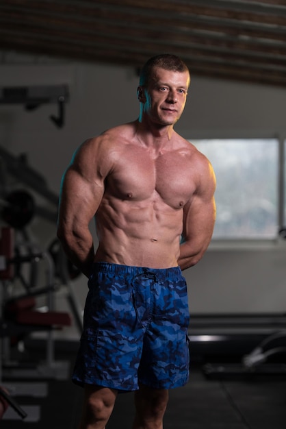 Bell'uomo in piedi forte in palestra e flettendo i muscoli Modello di fitness bodybuilder atletico muscolare in posa dopo gli esercizi