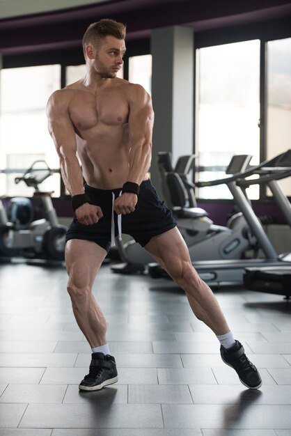 Bell'uomo in piedi forte in una moderna palestra e flettendo i muscoli Muscoloso atletico culturista modello di fitness in posa dopo gli esercizi