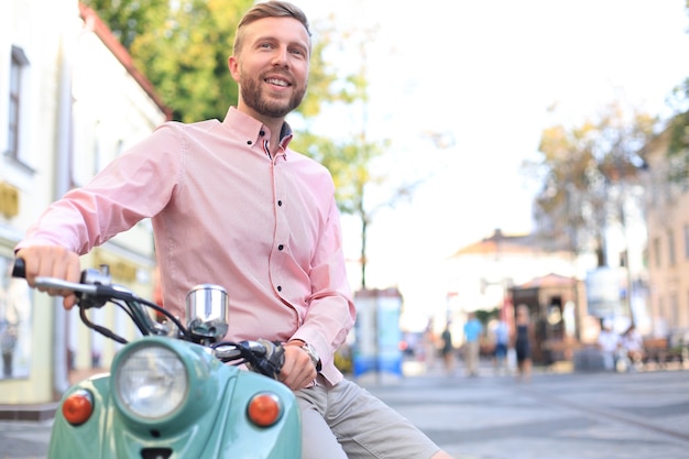 Bell'uomo in posa su uno scooter in un contesto di vacanza. Moda e stile di strada.