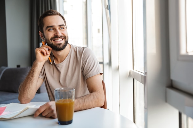 Bell'uomo intelligente felice che prende appunti mentre è seduto al tavolo a casa