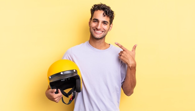 Bell'uomo ispanico che sorride con sicurezza indicando il proprio concetto di casco da moto con ampio sorriso