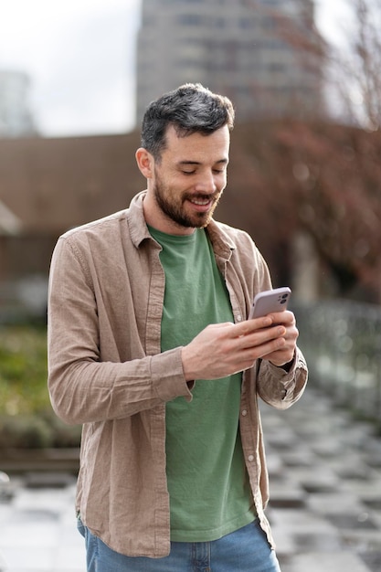 Bell'uomo latino che tiene il cellulare leggendo un messaggio di testo in piedi sulla strada