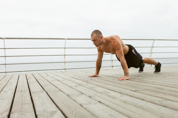 Bell'uomo muscoloso con il torso nudo che fa esercizio di push-up sulla spiaggia