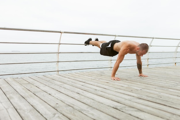 Bell'uomo muscoloso con il torso nudo che fa esercizio di push-up sulla spiaggia