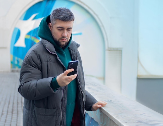 Bell'uomo serio che guarda il telefono cellulare nel paesaggio urbano all'aperto