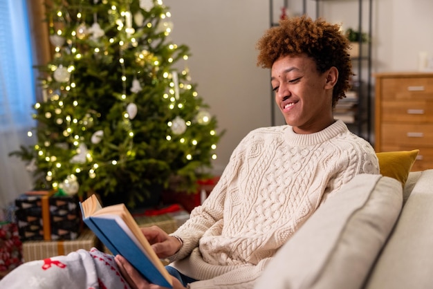 Bell'uomo sorridente amichevole in maglione si siede rilassante sul divano leggendo un libro accogliente festosa casalinga