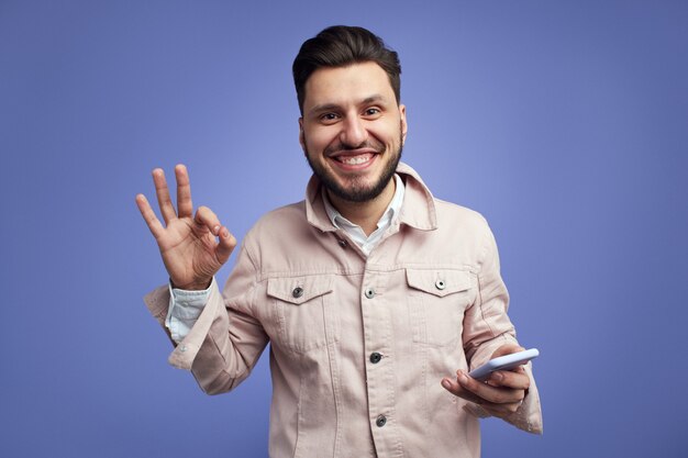 Bell'uomo sorridente e gesticolando segno ok mentre tiene il cellulare