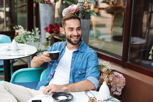 Bell'uomo sorridente seduto al tavolino del bar all'aperto, bevendo caffè